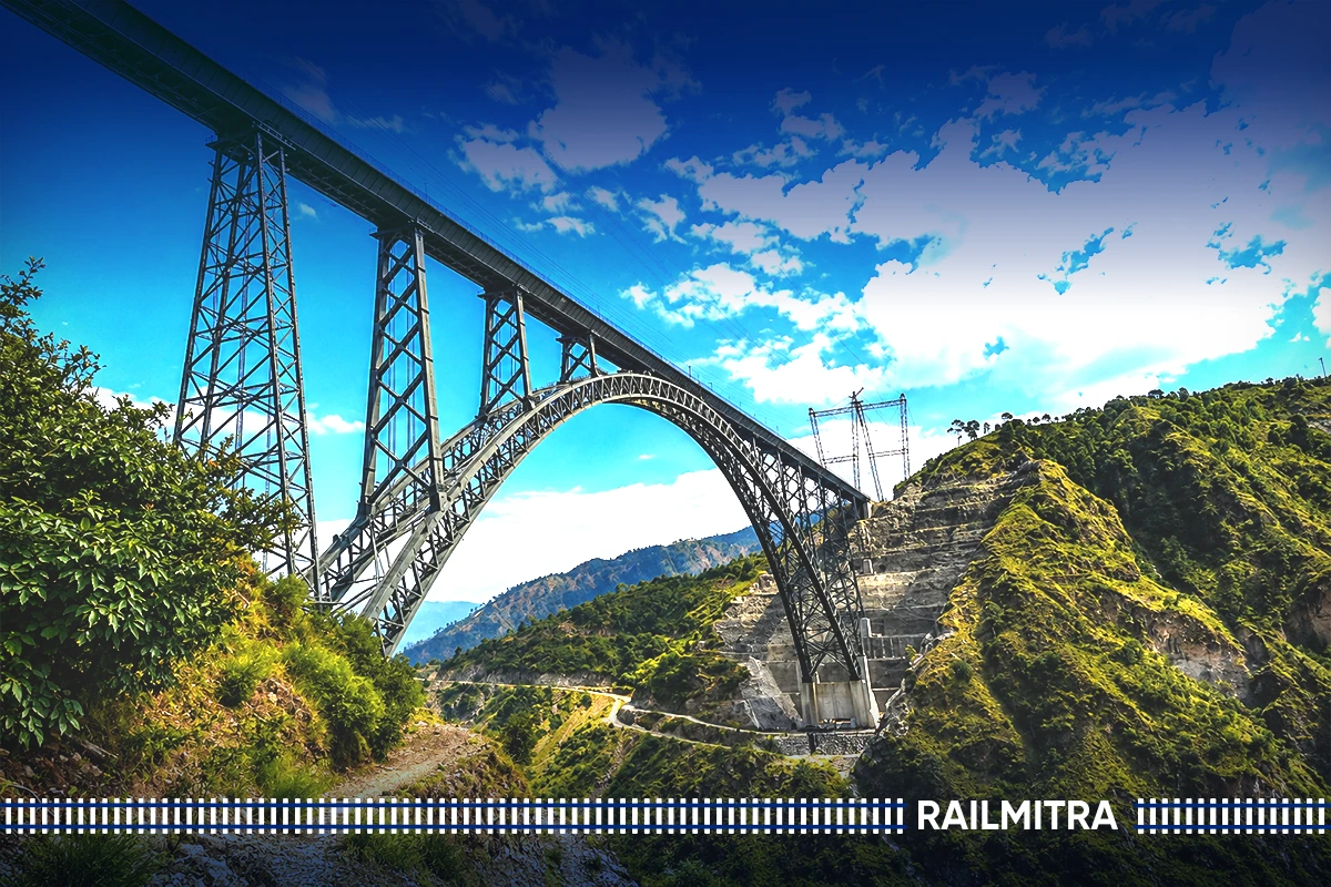 Architectural view of the Chenab Bridge steel arch engineering design spanning across a lush green Himalayan valley under a blue sky.